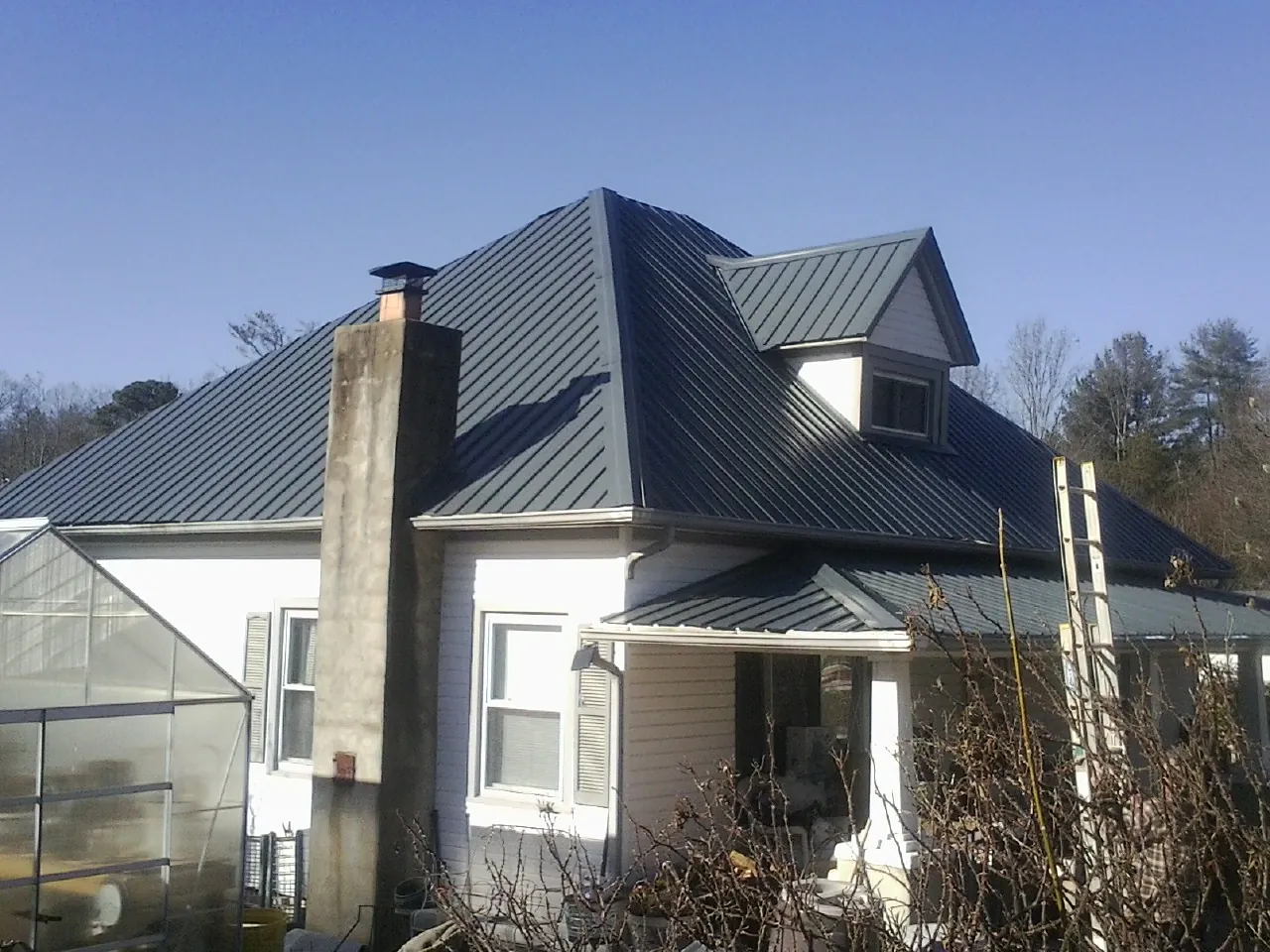 Dark blue standing seam metal roof on a white farmhouse with dormer — Slate & Tile Roof Repair by Roofing Brothers in Toddville