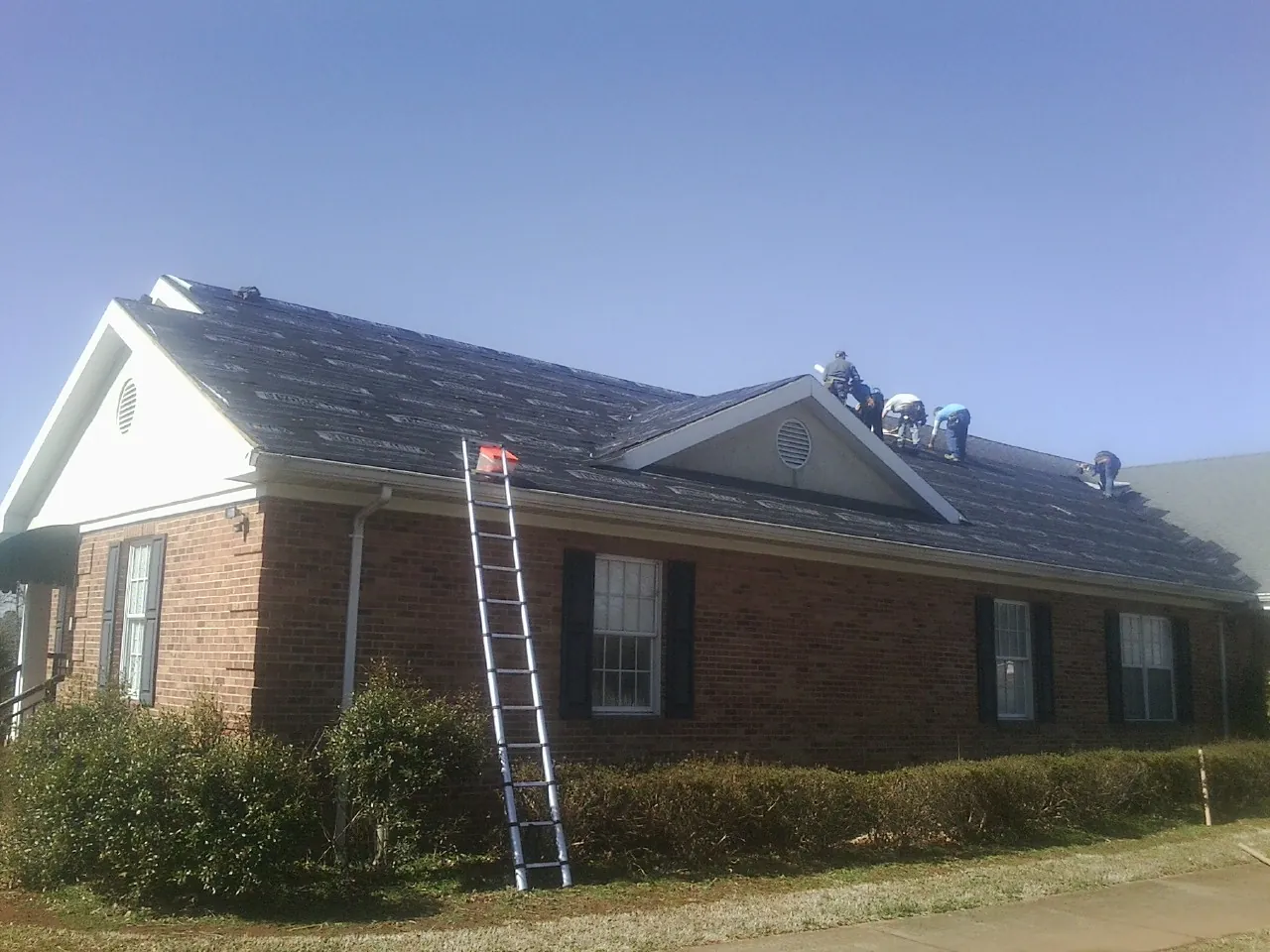 Crew tearing shingles off a brick ranch roof with a ladder set — Metal Roof Repair work by our crew in Toddville