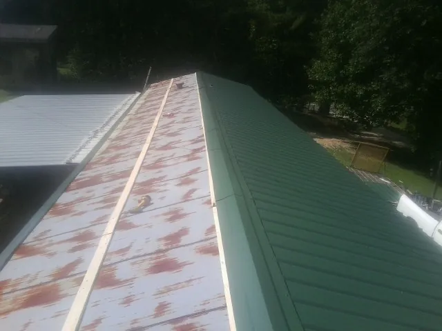 Old rusted panels beside newly installed green metal roofing — Wind Damage Roof Repair by Roofing Brothers in Toddville