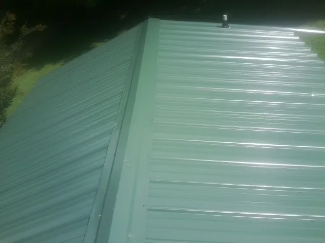 New green metal panels meeting at the ridge of a roof — Flat Roof Repair work by our crew in Toddville